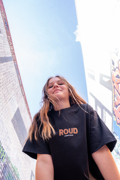 Person wearing a black t-shirt with 'ROUD' logo against a colorful mural.