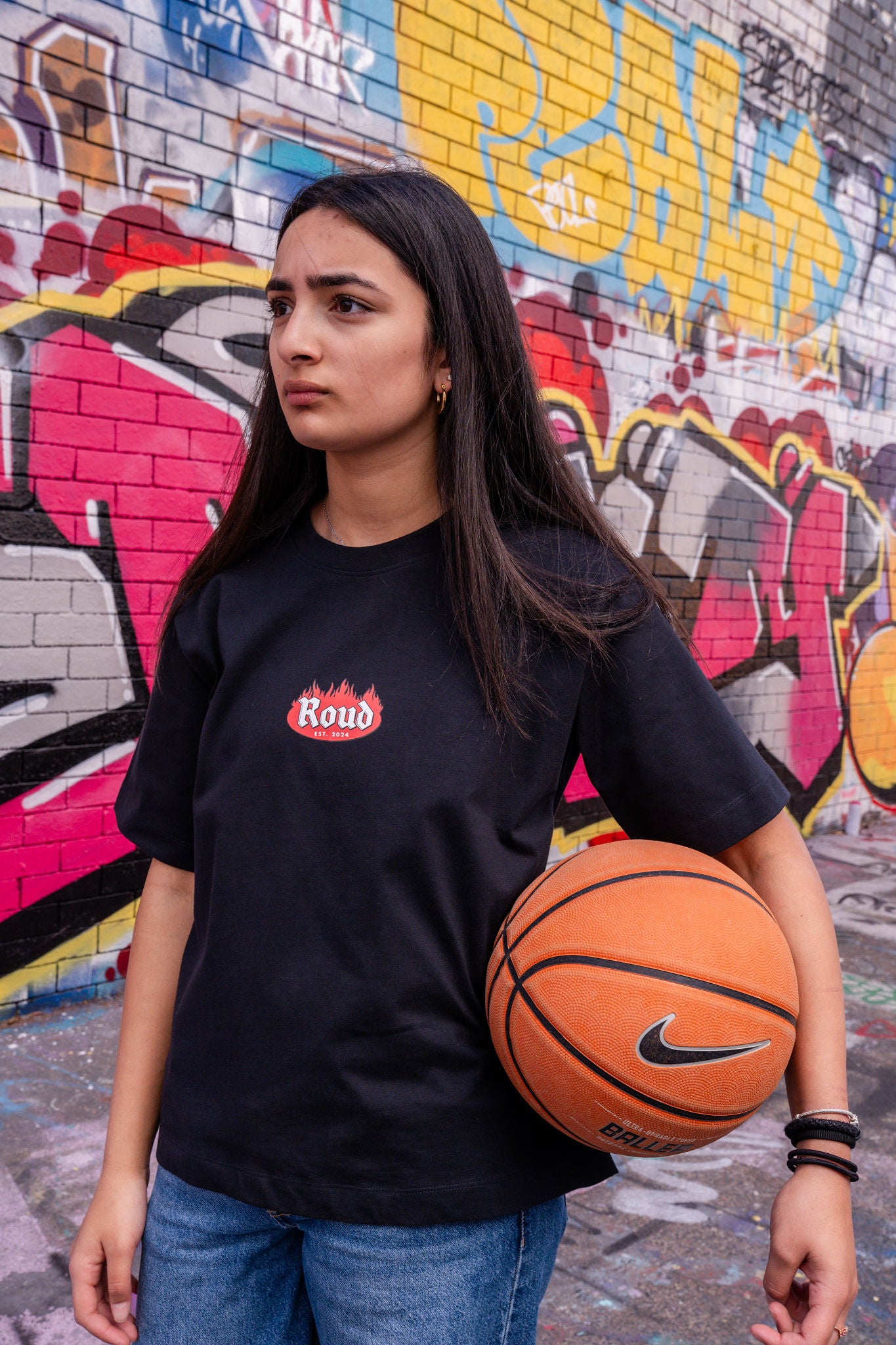 Person holding a basketball in front of a graffiti-covered wall
